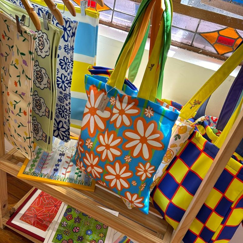 Retail display of colorful tote bags and placemats with floral and animal patterns, commercial art licensing showcase by Mirador Art Studio.