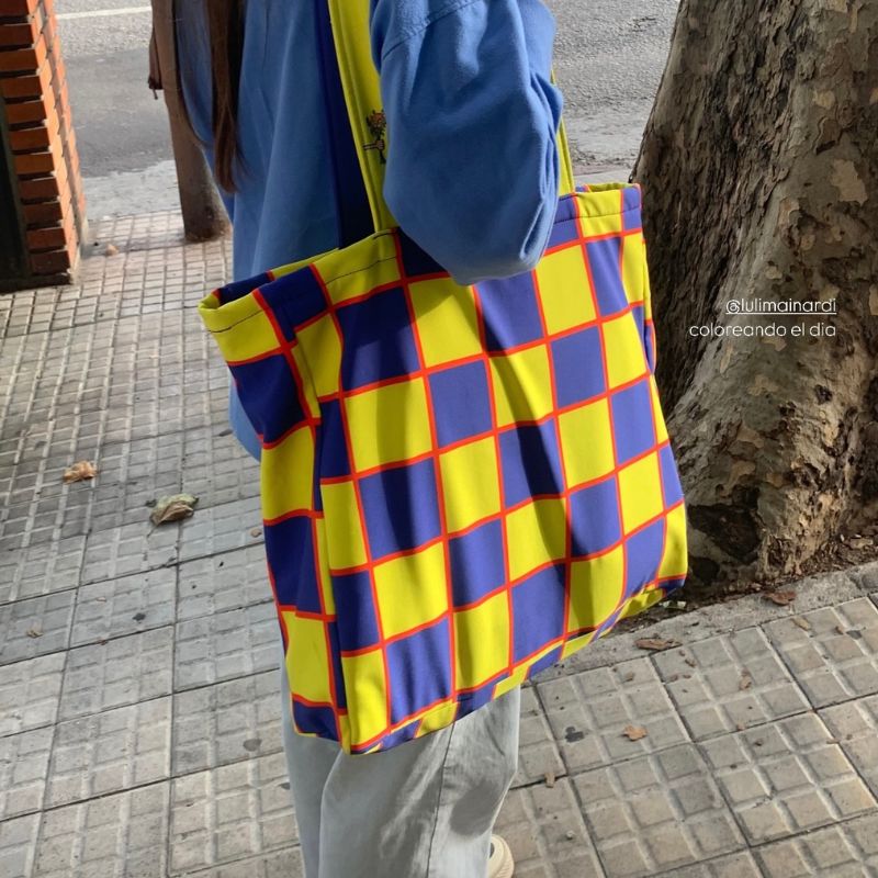 Woman carrying a yellow and blue checkerboard pattern tote bag, vibrant textile design and fashion licensing example by Mirador Art Studio.