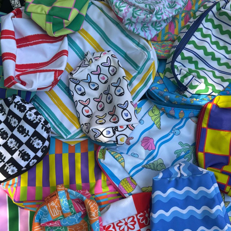 Flat lay of various artistic zipper pouches with fish, floral, stripes, geometric and shell patterns, colorful surface design portfolio by Mirador Art Studio.