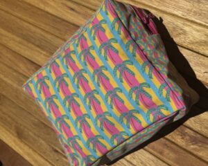 Neceser grande de tela impermeable y diseño de palmeras sobre rayas coloridas.